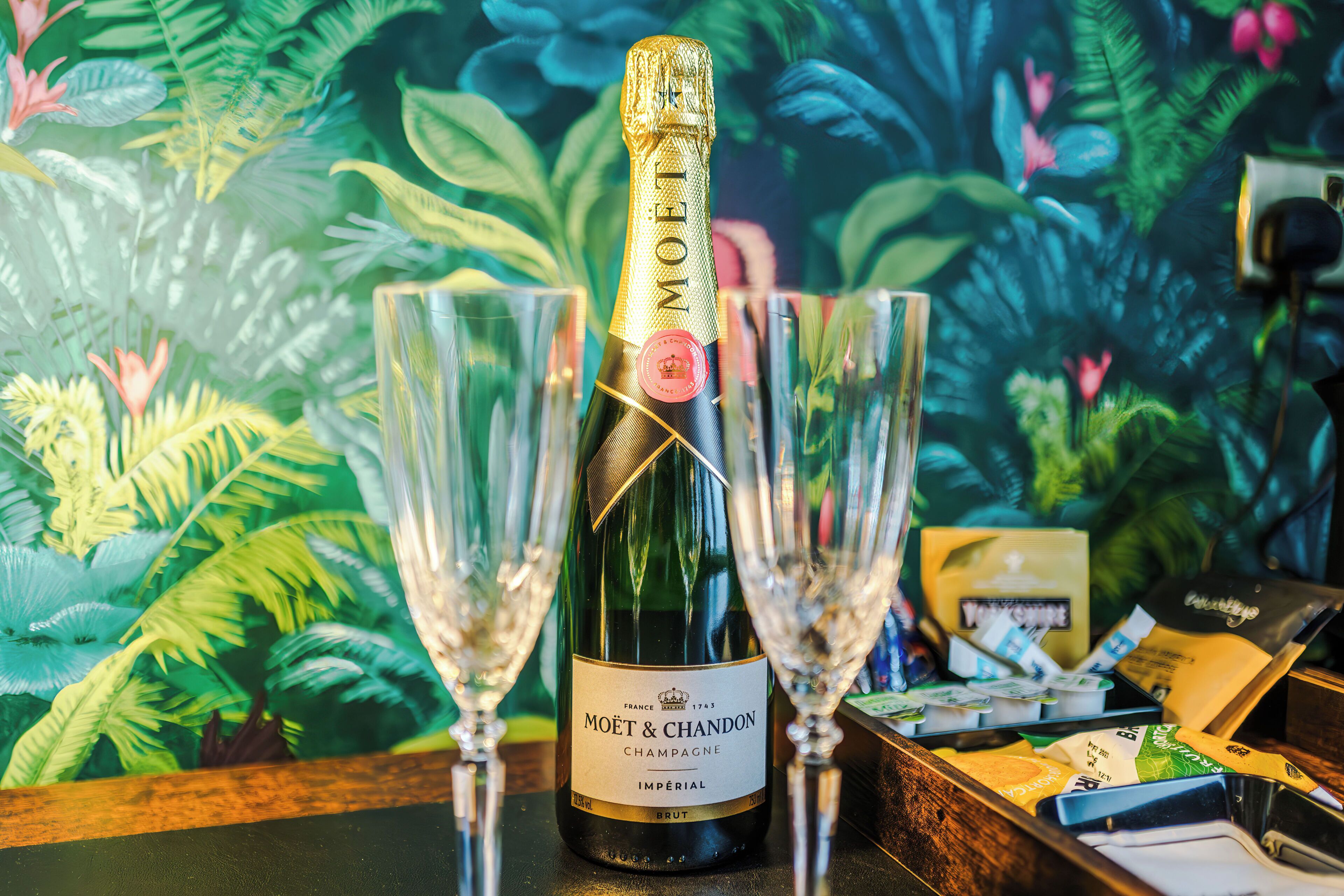 A bottle of Moët & Chandon champagne with two glasses, set against a tropical wallpaper backdrop.