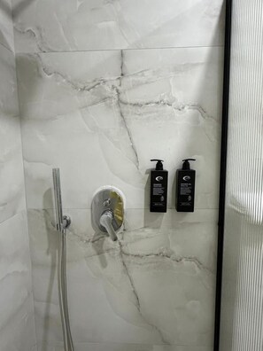 Kylpyhuone, jossa on marmoriseinä, suihku sekä kaksi mustaa pulloa shampoota ja suihkugeeliä.
