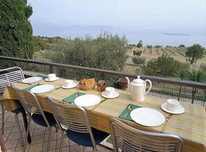 Ein Esstisch im Freien mit Stühlen, Blick aufs Meer und einem Zaun.
