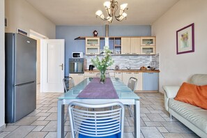 Eine moderne Küche mit Essbereich, ausgestattet mit einem Glastisch, Metallstühlen und einem Kronleuchter.
