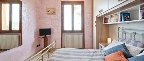 A bedroom with a bed, a television, a bookshelf, and a window.
