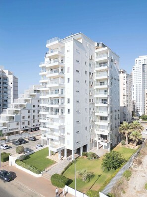 A multi-story residential building with balconies, a parking area, and a well-maintained lawn. - Stunning Sea View 3BDR With Terrace By Isrentals (Netanya)