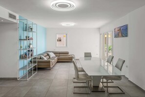 A modern living room with a glass dining table, leather sofa, and a blue shelving unit. - Stunning Sea View 3BDR With Terrace By Isrentals (Netanya)