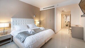 Una habitación de hotel moderna con una cama grande, una mesita de noche con lámpara, un armario y un televisor montado en la pared.