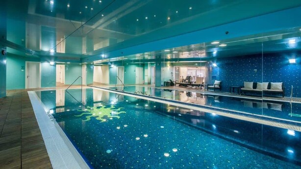 Una piscina interior con agua cristalina, una zona de terraza de madera y un área de descanso con cojines.