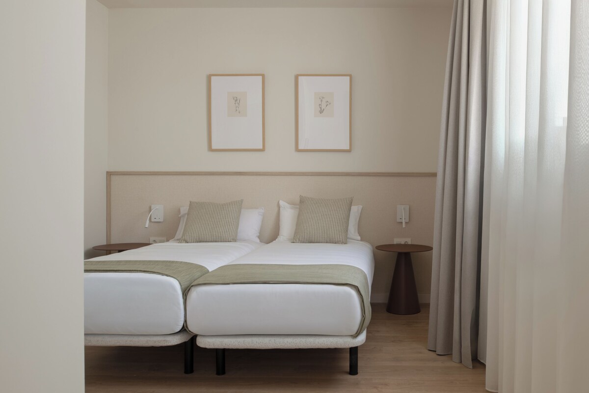 A double bed with two pillows, a bedside table, a wall-mounted light, and two framed pictures.