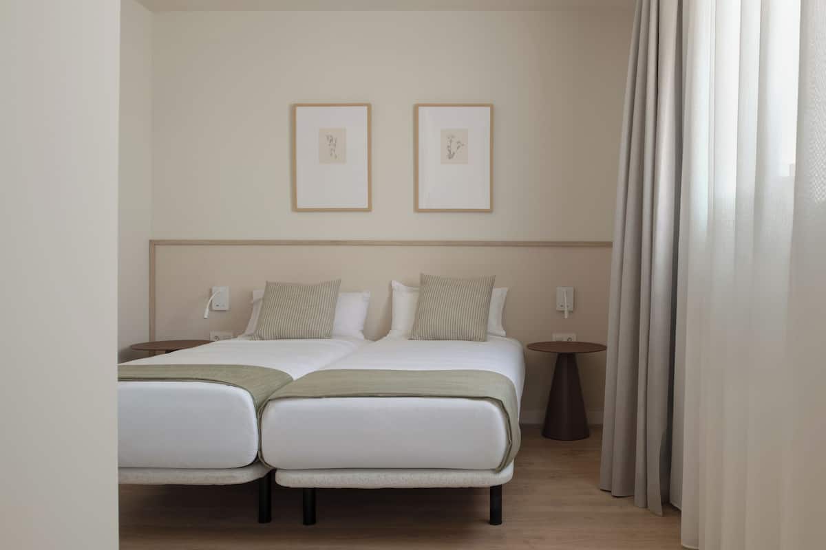 A double bed with two pillows, a bedside table, a wall-mounted light, and two framed pictures.