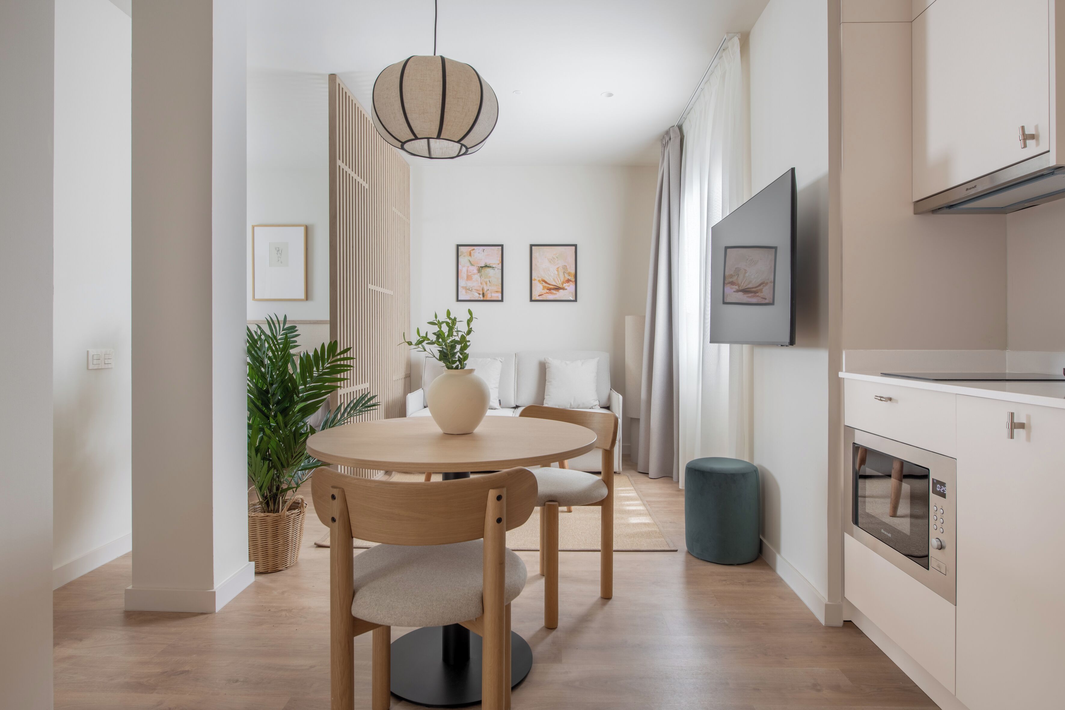 A modern kitchen with a built-in oven, a dining area with a round table and chairs, and a large TV mounted on the wall.