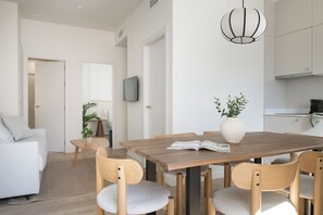 A modern living room with a dining table, chairs, a sofa, a TV, and a kitchen area.