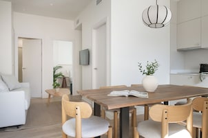 Una sala de estar moderna con una mesa de comedor, sillas, un sofá, un televisor y una cocina.