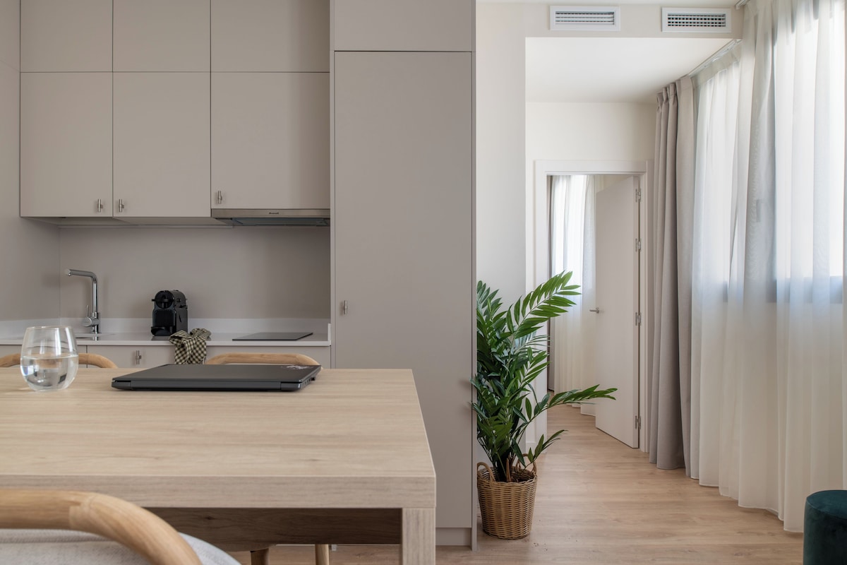 Una cocina moderna con armarios blancos, una mesa de comedor con sillas, una computadora portátil y una planta en maceta.