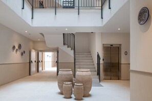 Un lobby amplio con escaleras, jarrones grandes y un moderno ascensor.