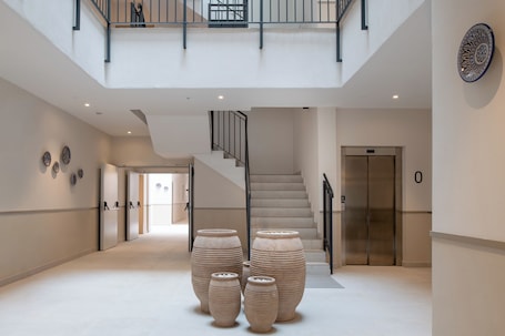 A spacious lobby with a staircase, large vases, and a modern elevator.