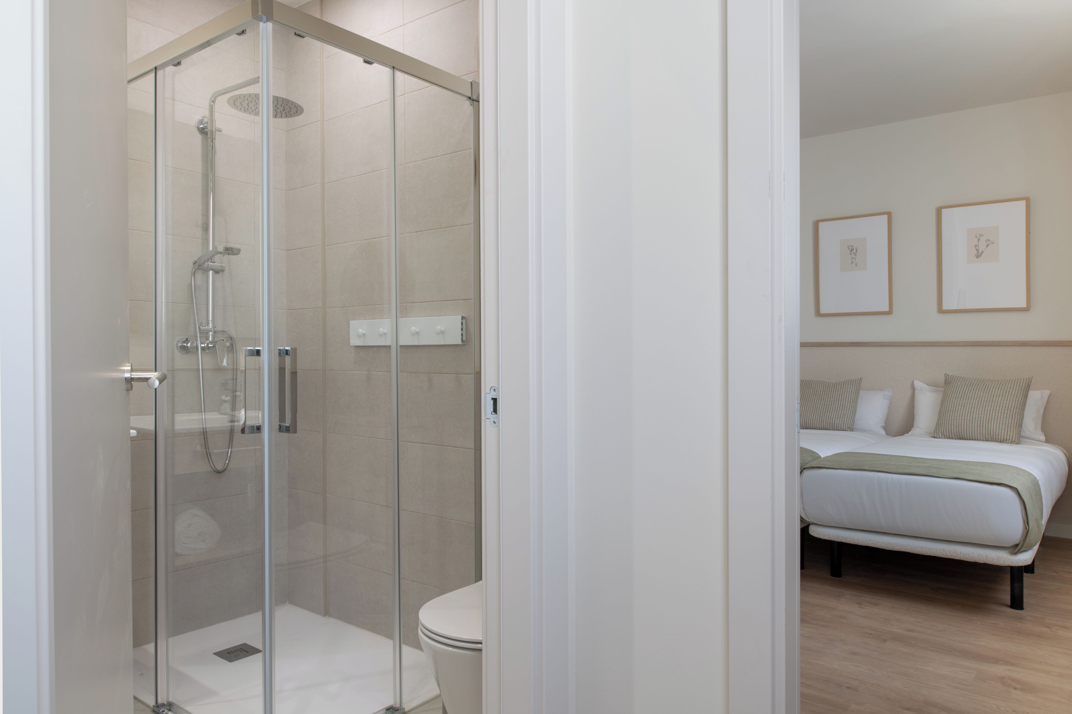 A modern bathroom with a glass-enclosed shower, a toilet, and a bed with a white mattress and pillows.