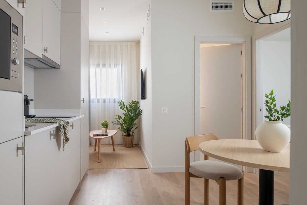 A modern kitchen with white cabinets, a built-in microwave, and a small dining area with a round table and chairs.