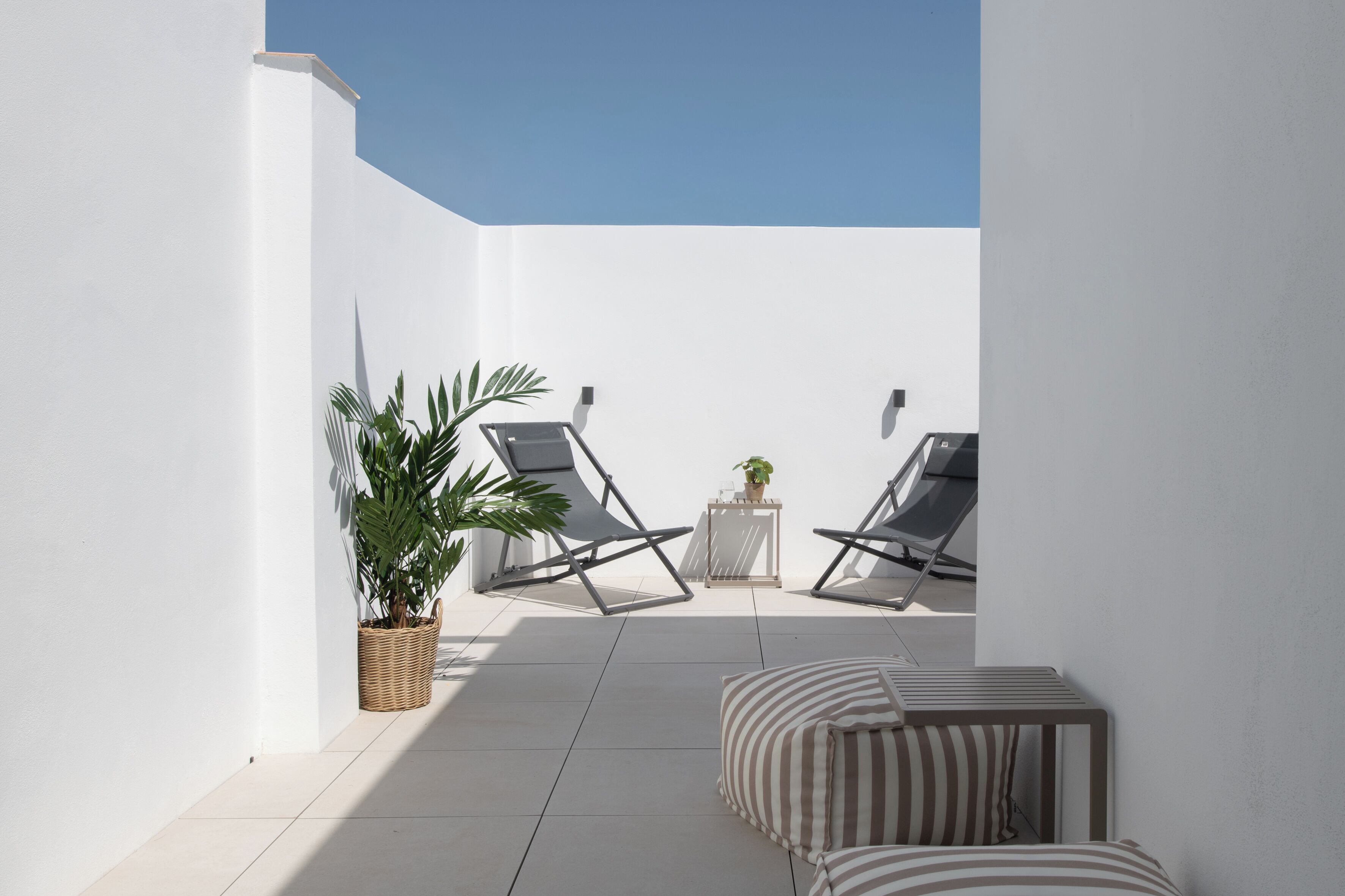 Un patio soleado con dos sillones, una mesita con una planta y un sofá a rayas.