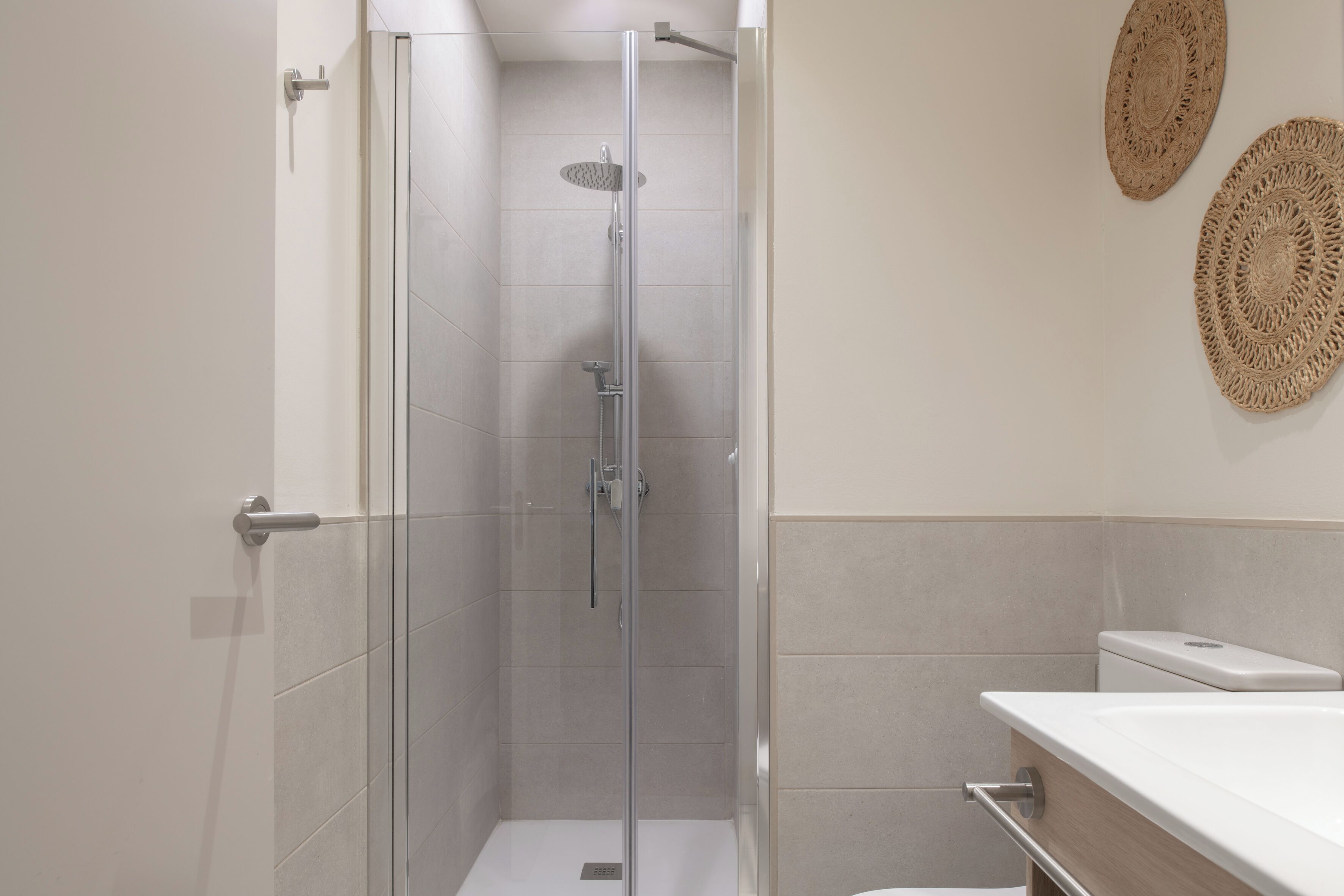 Un baño moderno con ducha de vidrio, un lavamanos blanco y dos adornos de pared tejidos.