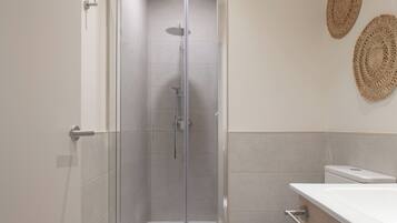Un baño moderno con ducha de vidrio, un lavamanos blanco y dos adornos de pared tejidos.