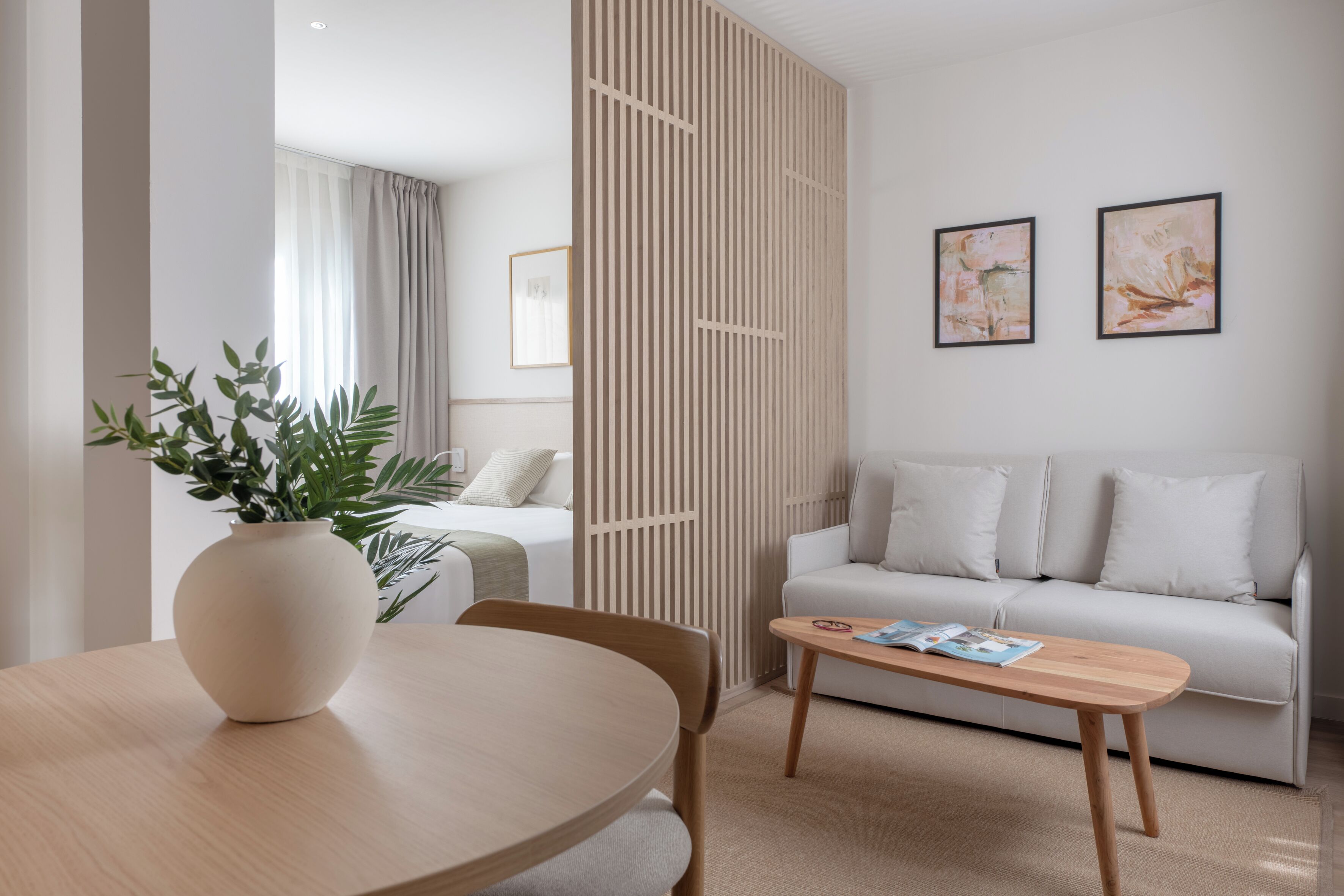 A modern living room with a round wooden table, a white sofa, and a decorative plant.