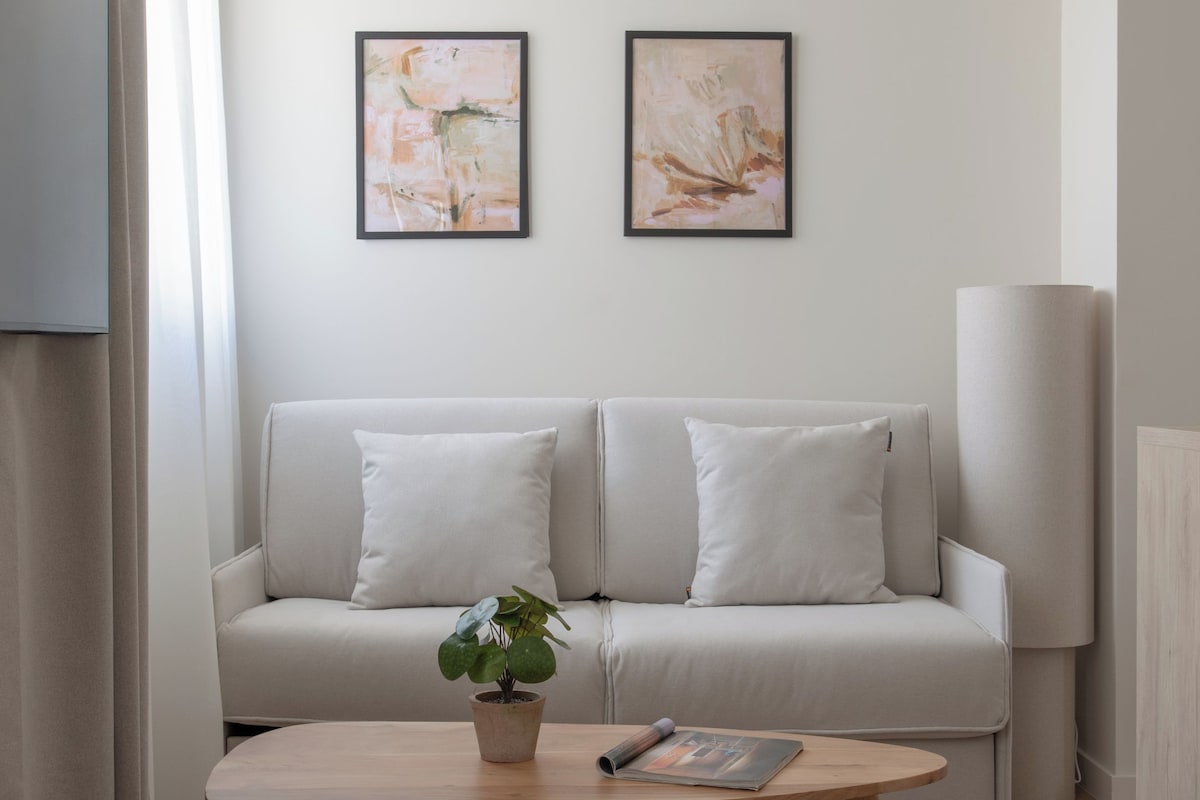 Una sala de estar con un sofá, dos cuadros abstractos enmarcados, una mesa de centro con una planta y una lámpara.