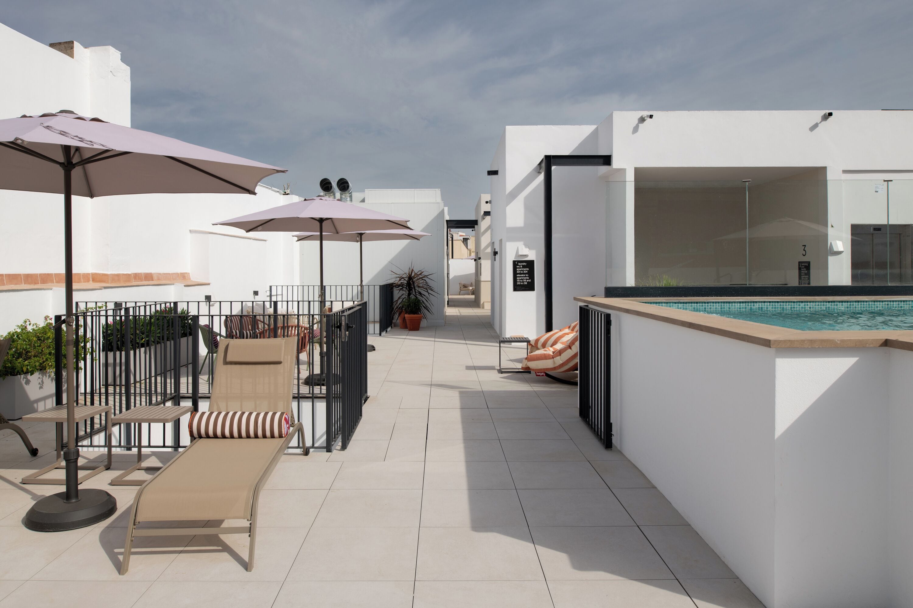A rooftop terrace with lounge chairs, umbrellas, and a swimming pool.