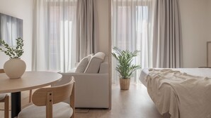 A modern hotel room with a round dining table, a sofa, a bed, and a potted plant. - Líbere Seville Triana (Seville)