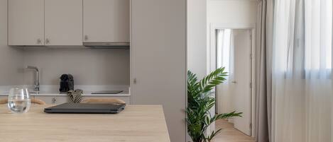 A modern kitchen with white cabinets, a dining table with chairs, a laptop, and a potted plant.