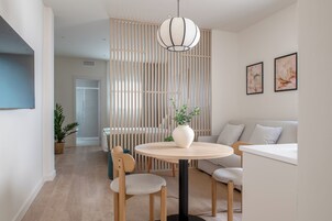 Una sala de estar moderna con una mesa redonda de madera, un sofá, una lámpara colgante y una planta decorativa.