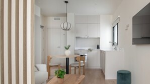 A modern kitchen with white cabinets, a dining area with a wooden table and chairs, and a small round stool. - Líbere Seville Triana (Seville)