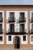 A multi-story building with a symmetrical facade, featuring a central arched entrance, evenly spaced windows, and balconies with wrought iron railings.