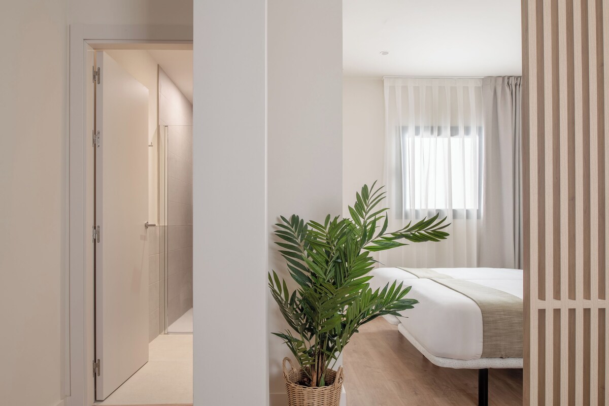A bedroom with a bed, a potted plant, and a window with curtains.