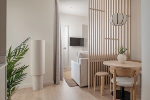 Una sala de estar moderna con un sofá, una mesa de comedor con sillas, un televisor montado en la pared y una planta decorativa.