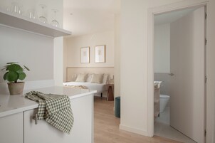 Una habitación de hotel moderna con cama, mesita de noche y una planta pequeña en maceta.