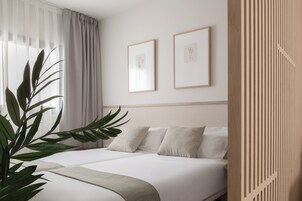 Habitación de hotel con una cama, dos cuadros en la pared, una planta en maceta y un separador de madera.