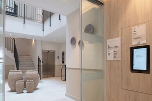 Un moderno vestíbulo de hotel con una escalera, jarrones decorativos, un quiosco digital de registro y un letrero que indica disponibilidad de WiFi.