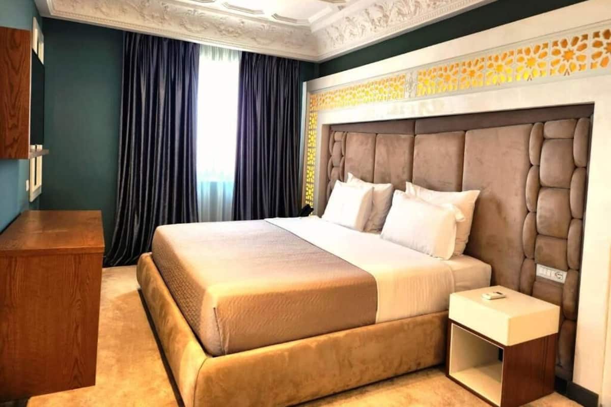 Habitación de hotel con una cama grande, una mesita de noche, un aparador de madera y un techo decorativo.