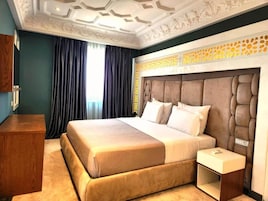 Habitación de hotel con una cama grande, una mesita de noche, un aparador de madera y un techo decorativo.
