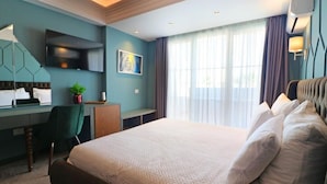 Habitación de hotel con una cama grande, un escritorio con silla, un televisor montado en la pared y una ventana con cortinas.