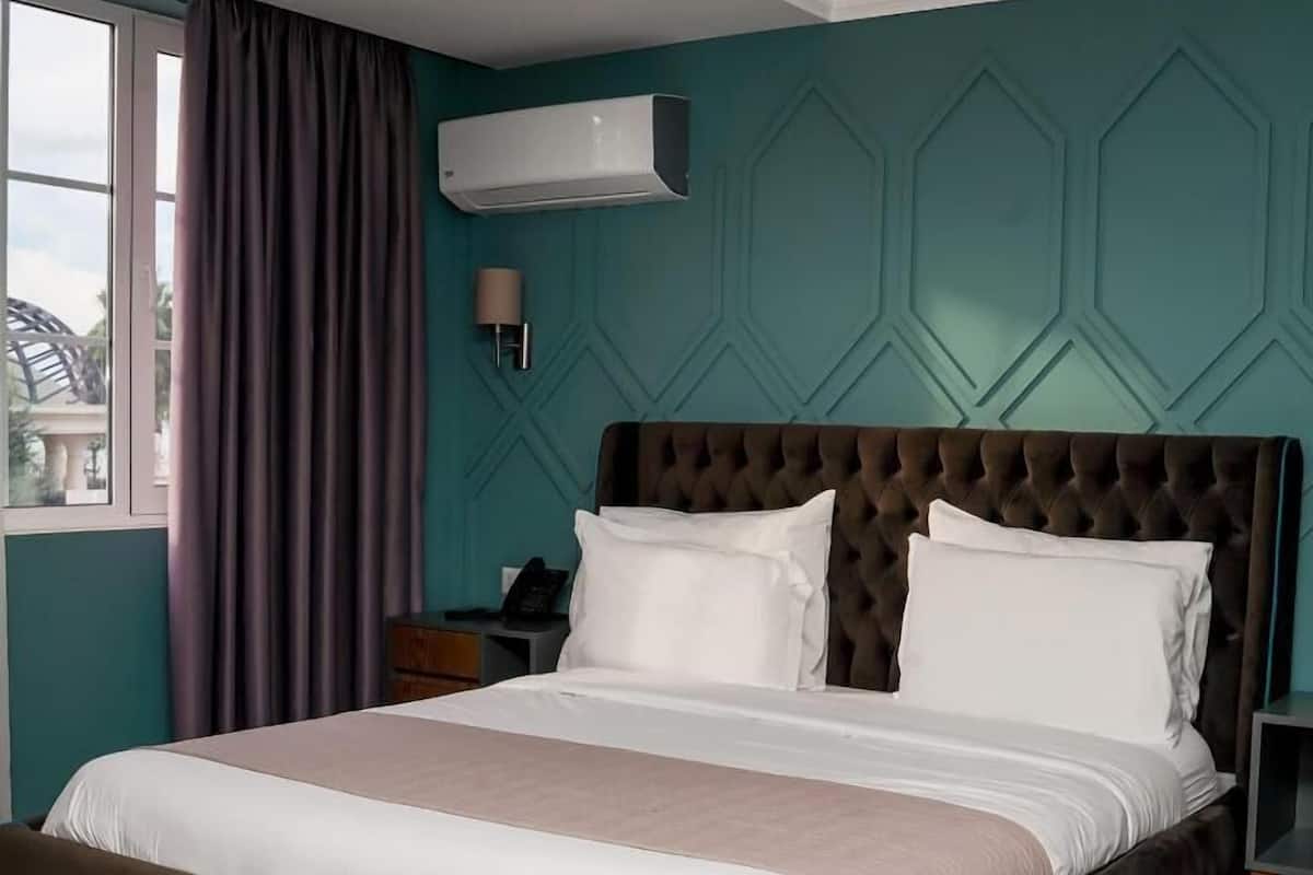 A hotel room with a large bed, a bedside table, a lamp, and a window with curtains.