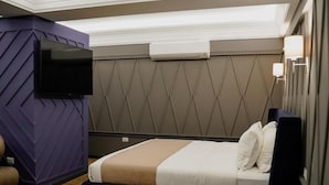 Habitación de hotel con cama, televisor de pantalla plana montado en la pared, mesita de noche y aire acondicionado mural.