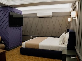 Habitación de hotel con cama, televisor de pantalla plana montado en la pared, mesita de noche y aire acondicionado mural.
