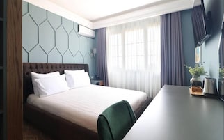 Una habitación de hotel con cama, escritorio, silla, televisor y ventana con cortinas.