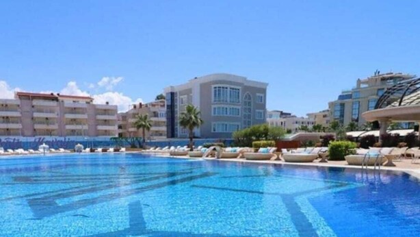 Una piscina con sillones de descanso, un edificio de varios pisos y palmeras.