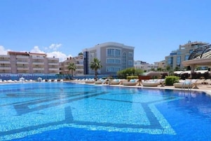 Una piscina con sillones de descanso, un edificio de varios pisos y palmeras.