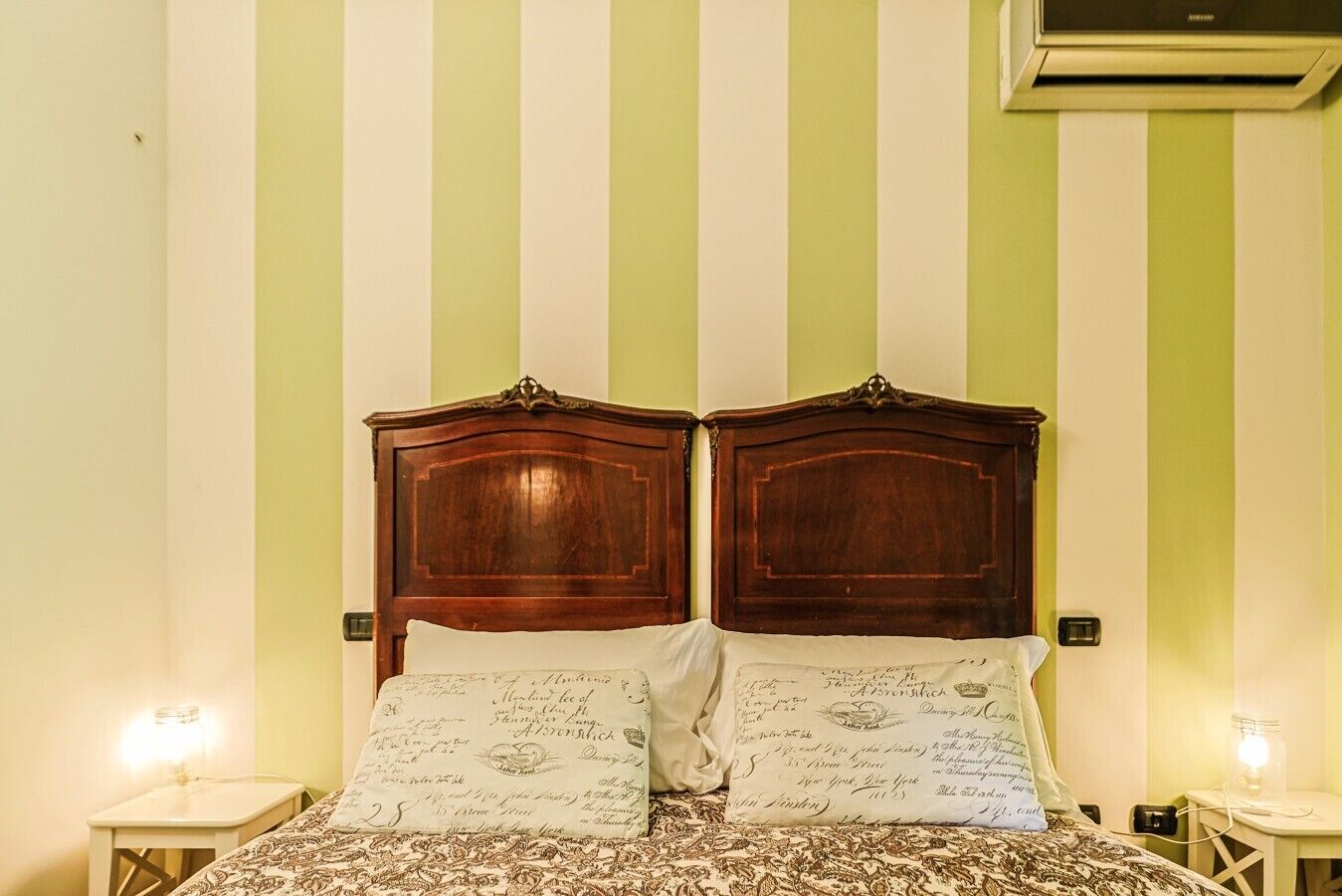 A bed with a wooden headboard, two bedside lamps, and a wall with vertical stripes.