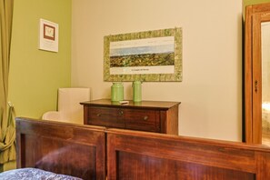 A room with a bed, a wooden dresser, a framed picture on the wall, and a green wall.