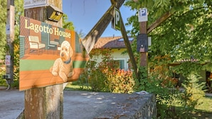 A sign for Lagotto House with a dog illustration, a parking sign, and a house in the background. - Lagotto House - Garden and Parking in the Langhe (Novello)