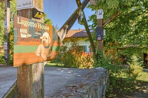 A sign for Lagotto House with a dog illustration, a parking sign, and a house in the background. - Lagotto House - Garden and Parking in the Langhe (Novello)