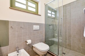 Un baño con inodoro, lavamanos y ducha con mampara de vidrio.
