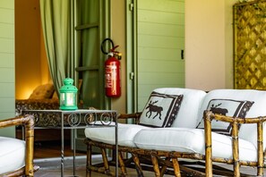 A room with a wicker sofa, a small table with a green lantern, and a fire extinguisher mounted on the wall. - Lagotto House - Garden and Parking in the Langhe (Novello)